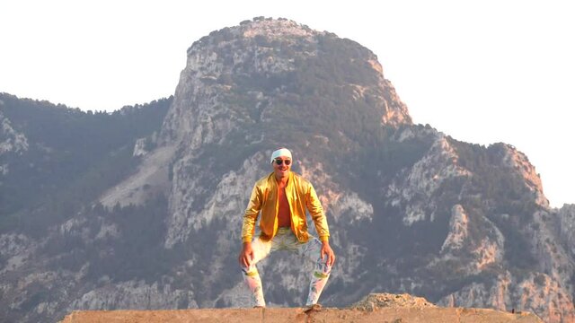 Young bald slender freak man caucasian in tight leggings, gold jacket, bandage on his head, dancing on roof at sunset, runs, has fun, behaves unusually. Slow motion video. Fun, humor, unusual people