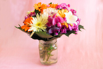 in a transparent glass vase there is a bouquet of bright summer flowers of white, pink, orange on a pink background . present