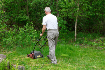 A man mows the lawn in the backyard with an electric lawn mower without collecting grass.
