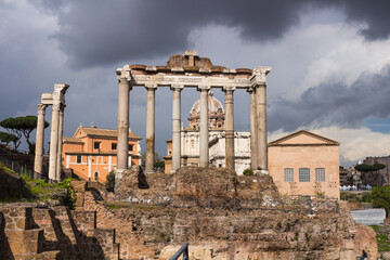 Roman forum in the sun against a dark, clouded sky. Ancient architecture and cityscape of historical Rome.