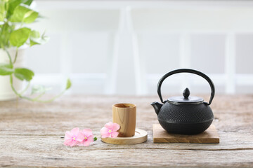 Black traditional teapot with wooden cup and pink flower on wooden table