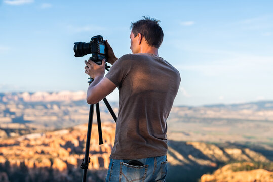 Man taking pictures photos of view from Bryce Point overlook of hoodoos rock formations in Bryce Canyon National Park at sunset with tripod and camera