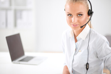 Portrait of smiling receptionist using laptop computer and headset at office desk