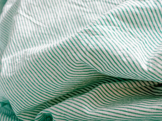 Close view of crumpled bedding. Green striped cotton fabric. Cloth washing and laundry concept at home. Change of bed linen to clean.