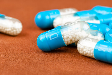Blue gelatin capsules with white granules inside, isolated on a brown background, macro shot.