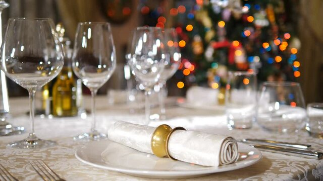 Restaurant concept. New Year and Merry Christmas feast table. Waiter in gloves serving dishes and wine glasses on table in background. Holiday tree lights blinking. 4 k