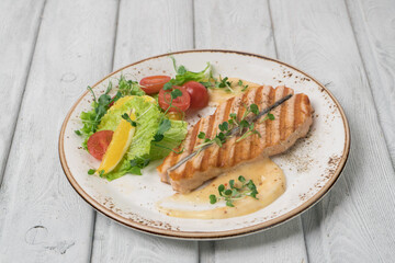 One piece of baked salmon grilled pepper lemon and salt on a white plate