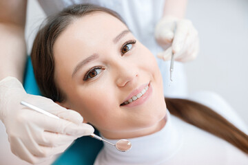 Patient in dental chair. Dentist's hands in gloves work with a dental tools. Beautiful young woman having dental treatment at dentist's office.