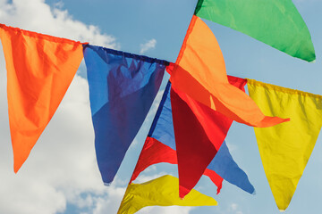On a sunny day, bright multi-colored flags are hung in the park. Blue sky with clouds.