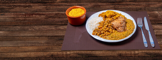 Delicious Caruru. Traditional Afro-Brazilian dish made with okra and dried shrimp, accompanied by vatapa, beans, rice, chicken and farofa. On a wooden table.