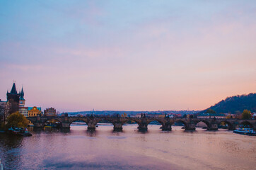 Fototapeta na wymiar Sundown in the Vltava River with a view to Charles Bridge and a gradient of purple to pink colors reflecting from the sky.