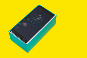 smartphone with a broken screen in a blue gift box on a yellow background