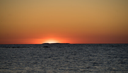 Orange sunset sky over Suur Strait. Nordic white night during Midsummer period. North coast of small Muhu island. Sun is just above the horizon, distinctive stripe over smooth water. Baltic sea.