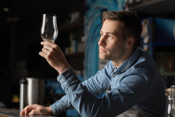 Pensive bartender looks at clean glass for beer, standing behind bar
