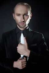 Portrait of businessman in black costume holding knife standing on dark background