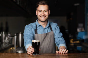 Fun in pub. Smiling bartender gives glass of dark beer