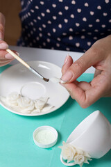 Roses with petals made of white polymer clay. A woman sticks them on a saucer. Crafts from polymer...