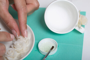Roses with petals made of white polymer clay. A woman sticks them on a saucer. Crafts from polymer...