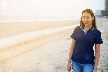 Portrait of young smiling  Asian woman standing on the beach embracing the golden sunshine glow of sunset. with copy space on left hand side.