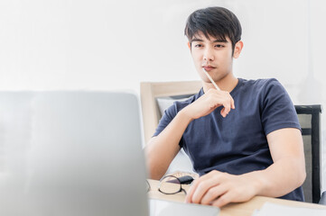 Young handsome student sitting at table and learning on line by laptop computer in bedroom