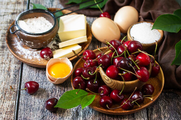 Cherry baking seasonal concept. Ingredients for cherry pie (red cherries, flour, eggs, sugar and butter) on a rustic wooden table.