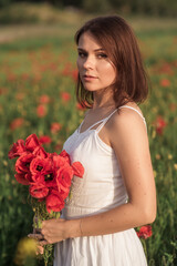 A girl in white dress holding a bouquet of poppies in a poppy field