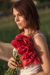 A girl in white dress holding a bouquet of poppies in a poppy field