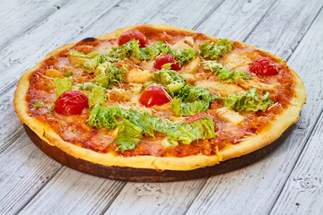 Fresh pizza with chicken, tomatoes and cheese on a light wooden background. Close-up, selective focus