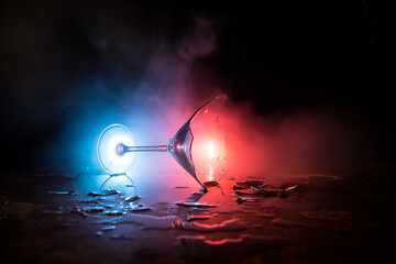 Broken glasses on wooden table at dark toned background with fog. Selective focus