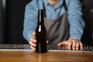 Service for client. Barman put on bar counter bottle of beer without label