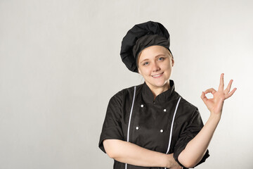 happy woman chef dressed in black uniform on a gray background. cooking concept. shows ok gesture.