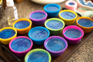 Colorful silicon cupcake molds on wooden coard filled with liquid soap for a home made hobby of melt and pour soapmaking