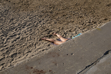 A pair of legs sticking out from the pier in famous italian beach in the Riviera Romagnola area, on the Adriatic coast. Catching sun.