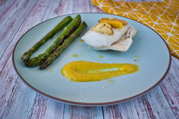 Top view of hake fillet with mango sauce and asparagus. Plate with warm colours and yellow background. Seafood dish