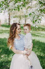 Close-up of a young woman and little boy in a park, outdoors. Mother holding her son, smiling, both wearing vintage clothes.