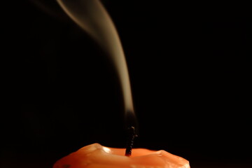 extinguished orange candle on a dark background with smoke detai
