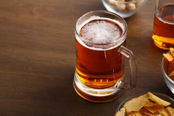 Bright ale mug for celebration. On brown wooden table is beer and chips