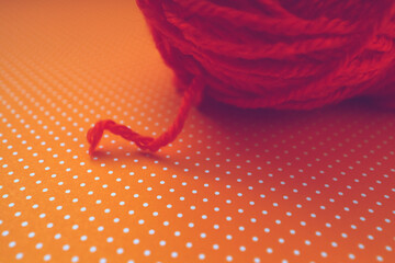 Orange yarn ball on an orange dotted background. 