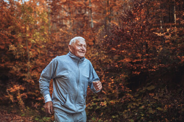 Naklejka na ściany i meble Senior runner in nature. Elderly sporty man running in forest during morning workout. Healthy and active lifestyle at any age concept