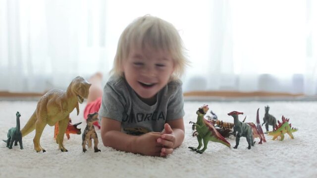 Blond toddler child, playing with dinosaurs at home, nice soft back light