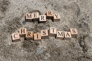Merry christmas text from wooden cubes. The cubes are on the beach sand.