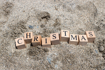 Merry christmas text from wooden cubes. The cubes are on the beach sand.