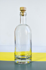 Empty transparent glass bottle. Bottle with cork, lit by the sun, stands on a gray-yellow background