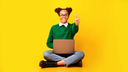 Happy afro teenager sitting with laptop with tumb up