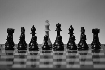 Black and white shot of a white king surrounded by black chess pieces on chessboard
