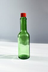 dark green decorative bottle with a red cap on a gray background, lit by the sun. Small green bottle for sauce