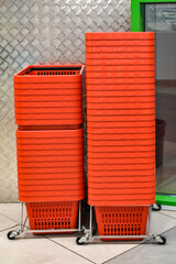 Red grocery baskets at the entrance to the supermarket. Empty red plastic shopping baskets are stacked in a row in front of the entrance to the supermarket.