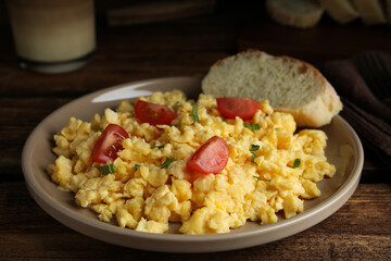 Tasty scrambled eggs with cherry tomato and bread on wooden table, closeup