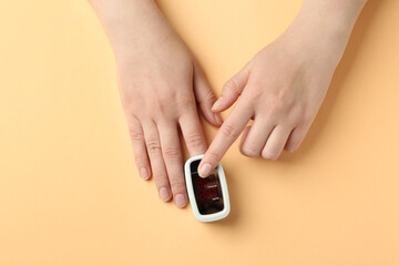 Woman using fingertip pulse oximeter on light orange background, top view