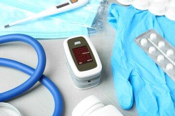 Modern fingertip pulse oximeter and medical items on light grey stone background